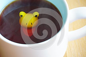 Cute yellow frog figurine in white cup of tea with baby blue base