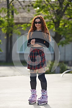 Cute young adult skater standing in a skatepark in modern aggressive inline skates on her feet. Cool tattooed female person