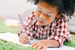 Cute young African American kid girl drawing or painting with colored pencil