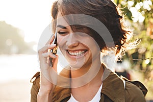 Cute young amazing woman walking outdoors in park in beautiful spring day talking by mobile phone