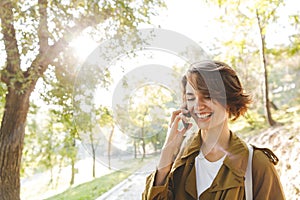 Cute young amazing woman walking outdoors in park in beautiful spring day talking by mobile phone