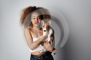 Cute young american african woman with curly hair hugging and kissing her puppy basenji dog. Love between dog and owner