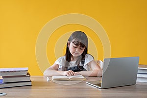 A cute young Asian girl focusing on reading a book at her study table. elementary school student