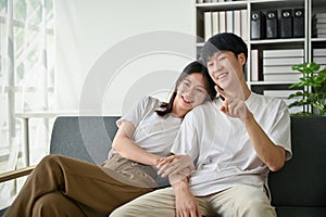 A cute young Asian girlfriend is hugging her boyfriend while enjoying watching TV on a couch