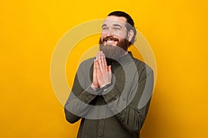 Cute young bearded man is holding hands together for a prayer or please.