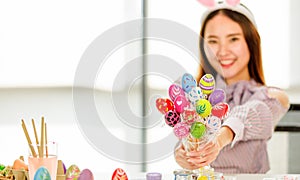 A cute young and beautiful Asian woman wearing bunny rabbit ears headband showing hand made painted easter eggs with happy and
