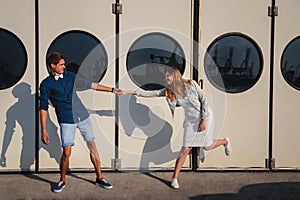 Cute young beautiful couple kidding at port, on the white wall with big portholes background, happy smiling outdoor portrait