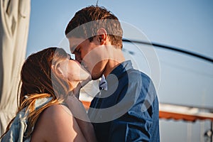 Cute young beautiful couple kissing near to the small summer cafe at port, happy smiling outdoor portrait