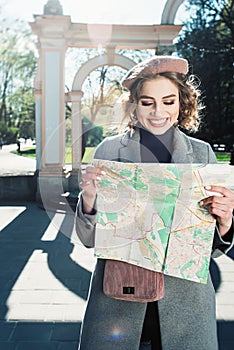 Cute young beautiful curly smiling caucasian travelling woman reading a map