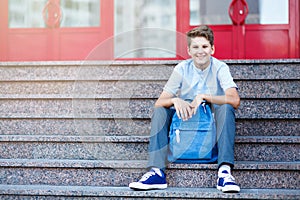 Cute, young boy in blue shirt with backpack sits on the steps before school. Education, Back to school