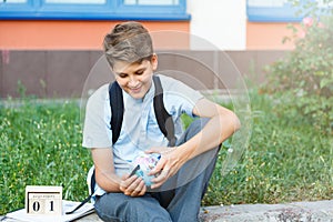 Cute, young boy in blue shirt with backpack stands in front of his school. Education, Back to school