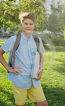 Cute, young boy in blue shirt with backpack and workbooks in his hands in front of his school. Education, Back to school