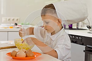 Cute young boy chef whipping the eggs