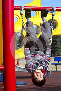 Cute young boy hanging upside down on a playground