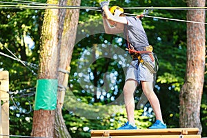 Cute young boy in helmet with climbing equipment in the rope amusement park. Summer camp