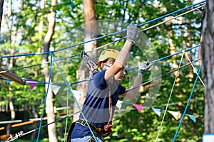 Cute young boy in helmet with climbing equipment in the rope amusement park. Summer camp