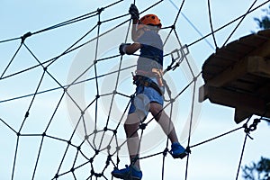 Cute young boy in helmet with climbing equipment in the rope amusement park. Summer camp,