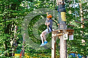 Cute young boy in helmet with climbing equipment in the rope amusement park. Summer camp,