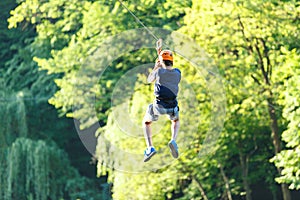 Cute young boy in helmet with climbing equipment in the rope amusement park. Summer camp,