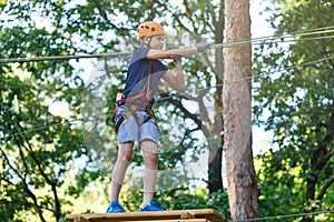 Cute young boy in helmet with climbing equipment in the rope amusement park. Summer camp