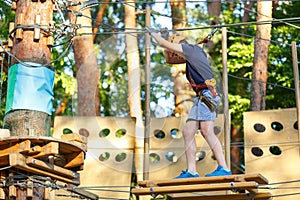 Cute young boy in helmet with climbing equipment in the rope amusement park. Summer camp