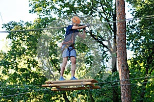 Cute young boy in helmet with climbing equipment in the rope amusement park. Summer camp,