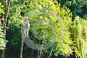 Cute young boy in helmet with climbing equipment in the rope amusement park. Summer camp