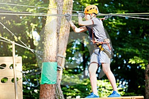 Cute young boy in helmet with climbing equipment in the rope amusement park. Summer camp, holidays