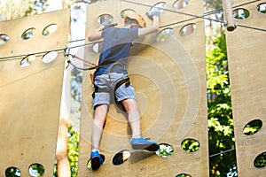 Cute young boy in helmet with climbing equipment in the rope amusement park. Summer camp, holidays
