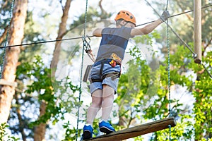 Cute young boy in helmet with climbing equipment in the rope amusement park. Summer camp, holidays