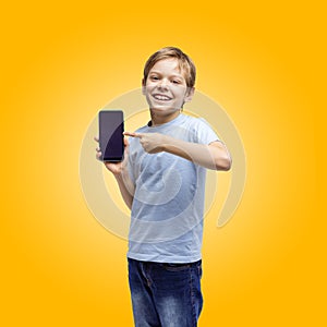 Cute young boy holding and pointing at smart phone, over yellow background, with path