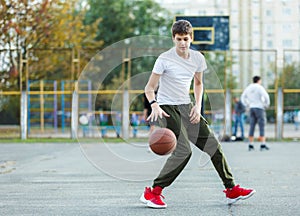 Cute young boy plays basketball on street playground. Teenager in white t shirt with orange basketball ball outside. Hobby,