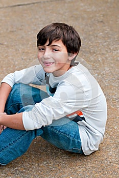 Cute young boy sitting on sidewalk looking at camera