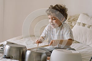 Cute young boy using wooden sticks to bang saucepans that are set up like a drumset