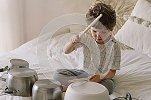 Cute young boy using wooden sticks to bang saucepans that are set up like a drumset