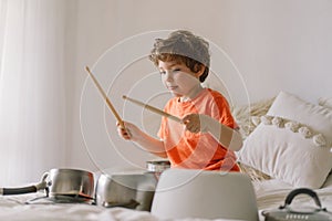 Cute young boy using wooden sticks to bang saucepans that are set up like a drumset