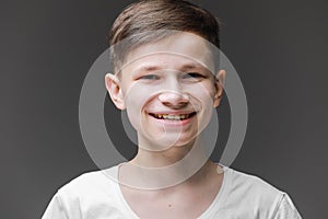 Cute young boy in white T-shirt posing in front of gray empty wall. Portrait of fashionable male child. Smiling boy posing, blank