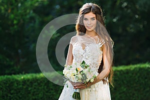 Cute young bride with long hairs holding her wedding bouquet includes white roses and other flowers. Beautiful white