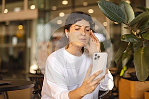 Cute young caucasian girl with cell phone in her hands browsing internet sitting in cafe.