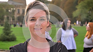 Cute young caucasian girl smiling focused in front of group of diverse women outdoor