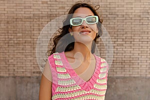 Cute young caucasian girl in sunglasses looking at camera with brick wall in background.
