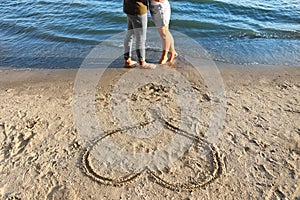 Cute young couple and drawing of heart on sea beach