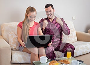 Cute young couple having breakfast, in front of laptop computer