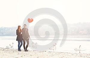 Cute young couple in love, walking at the riverside, with a red balloon