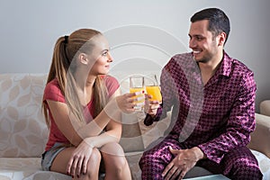 Cute young couple sitting on sofa and drinking orange juice.