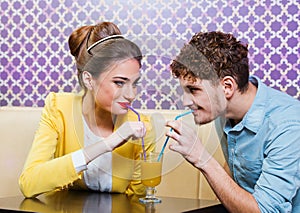 Cute young couple sitting at the table sharing a drink