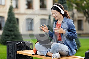Cute young eastern woman student using laptop and headphones outdoors