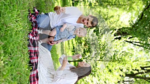 Cute young family blowing soap bubbles, sitting on a blanket in park,playing,having fun together on a warm sunny weekend