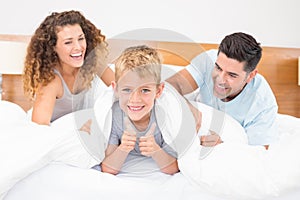 Cute young family messing about on bed with little boy showing thumbs up