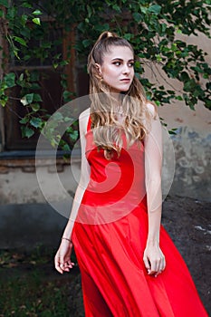 A cute young girl with blond flowing long hair and beautiful make-up, in a long red dress